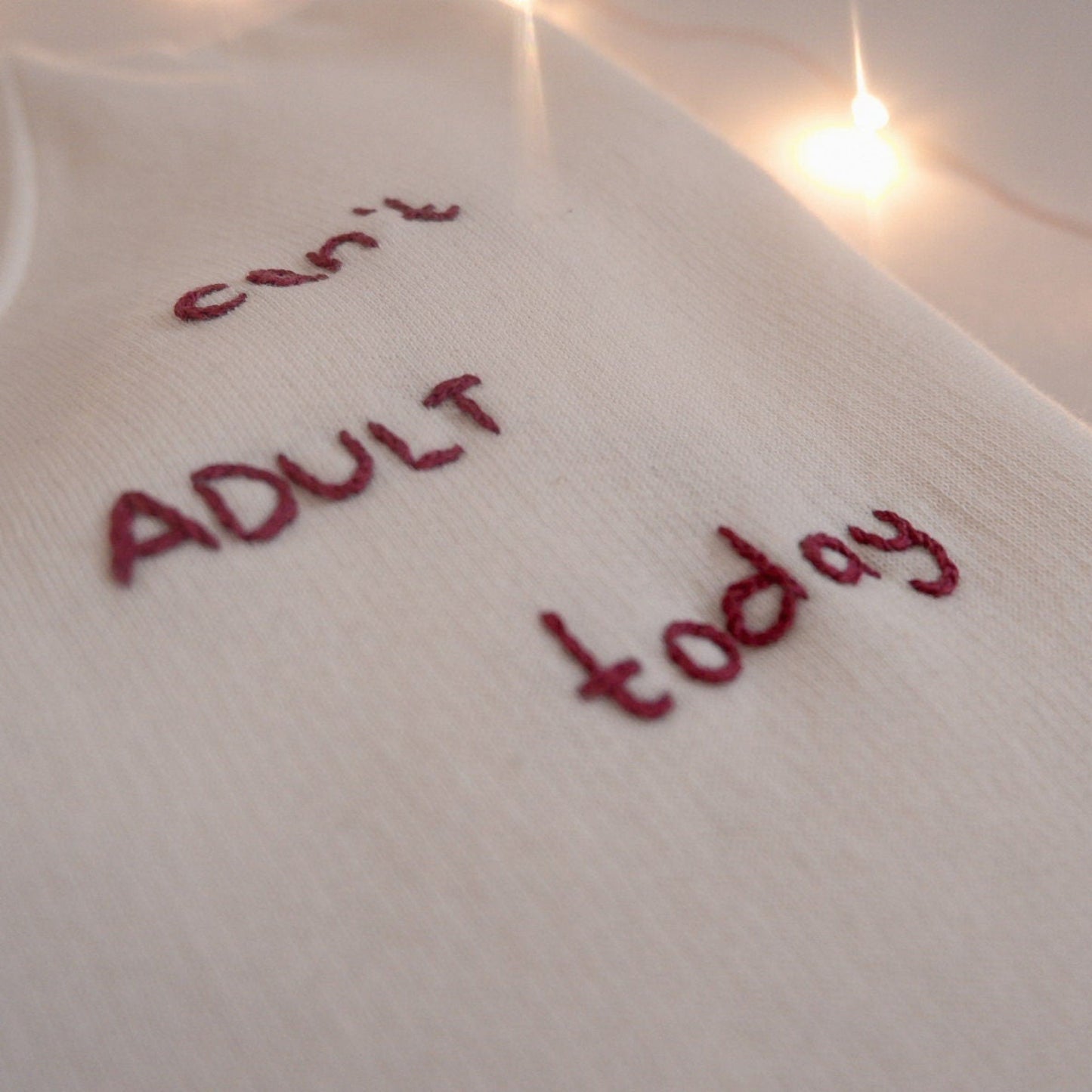 White sweatshirt with red text 'can't ADULT today' on a soft focus background