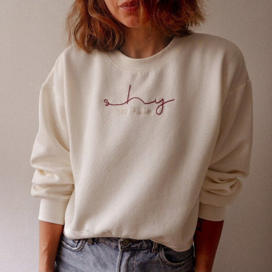 Person wearing a white sweatshirt with 'shy' text on a plain background