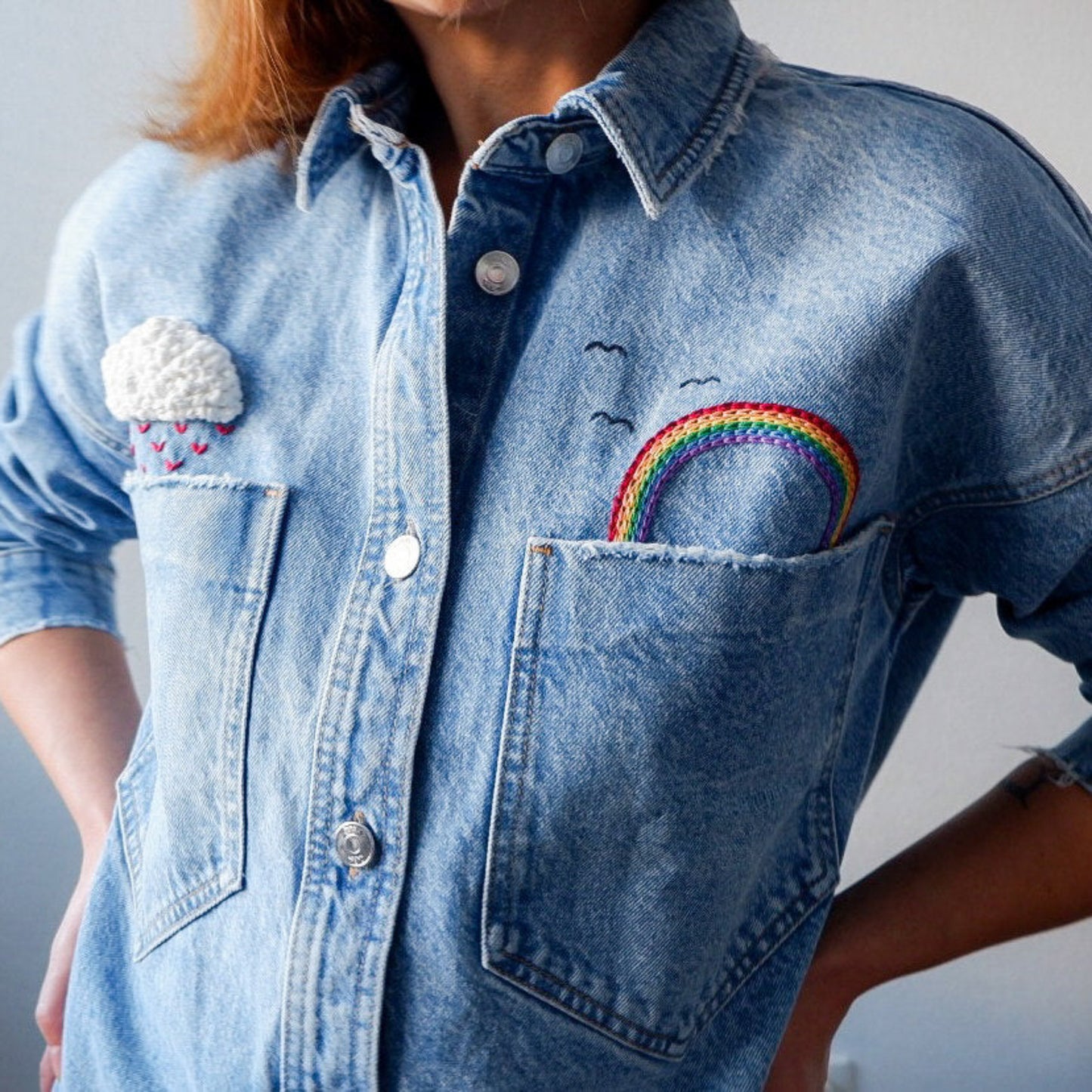 Person wearing a denim shirt with embroidered designs on a plain background