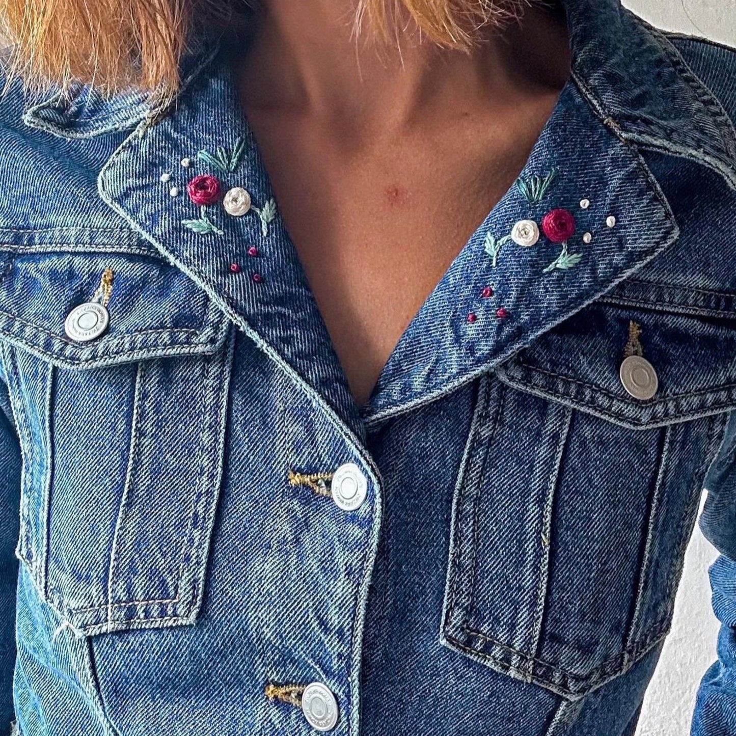 Close-up of a blue denim jacket with floral embroidery on a plain background