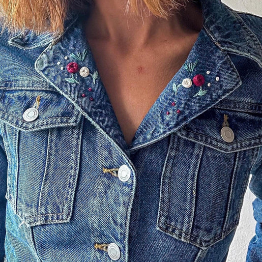 Close-up of a blue denim jacket with floral embroidery on a plain background