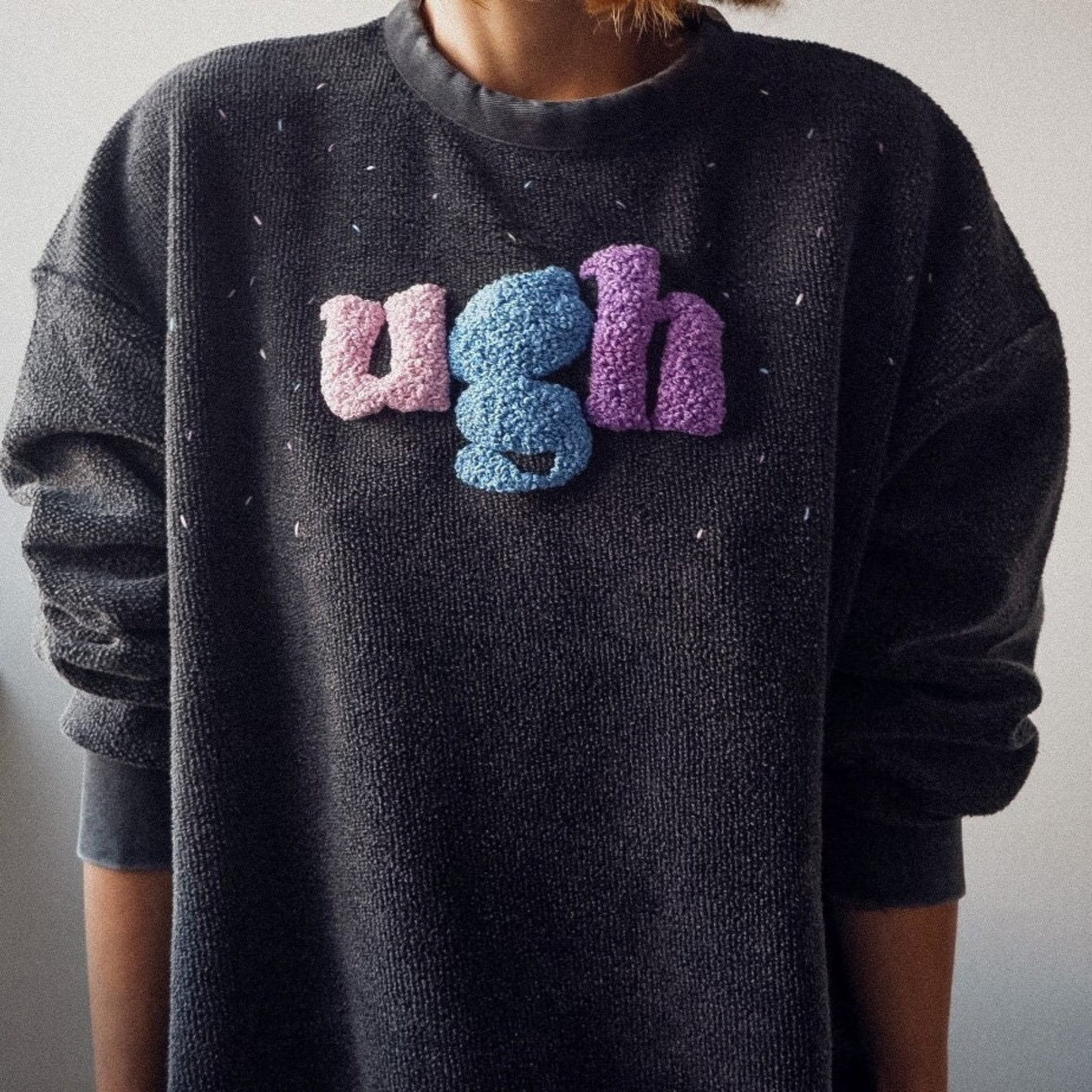 Black sweater with colorful 'ugh' text on a plain background