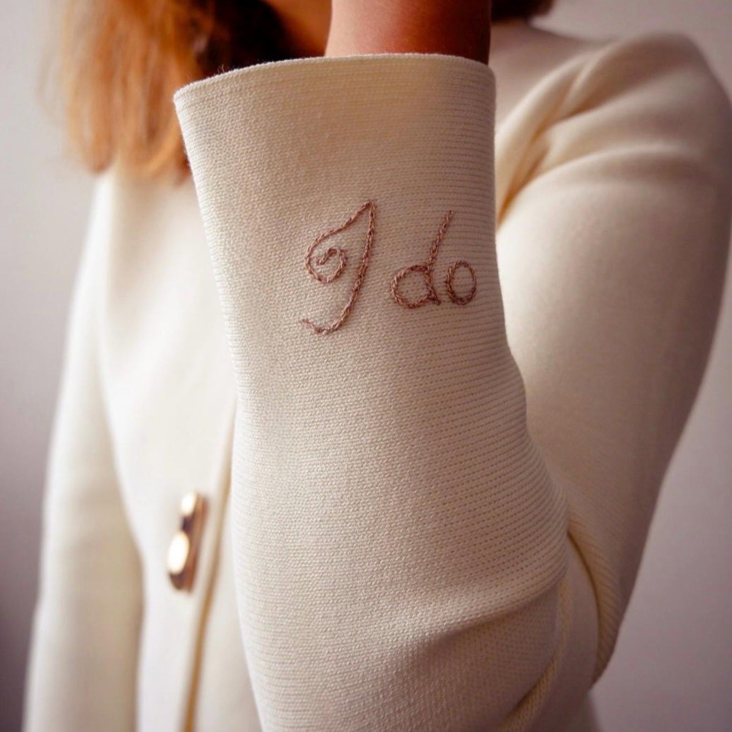 White sleeve with 'I do' embroidery worn by a person, against a neutral background