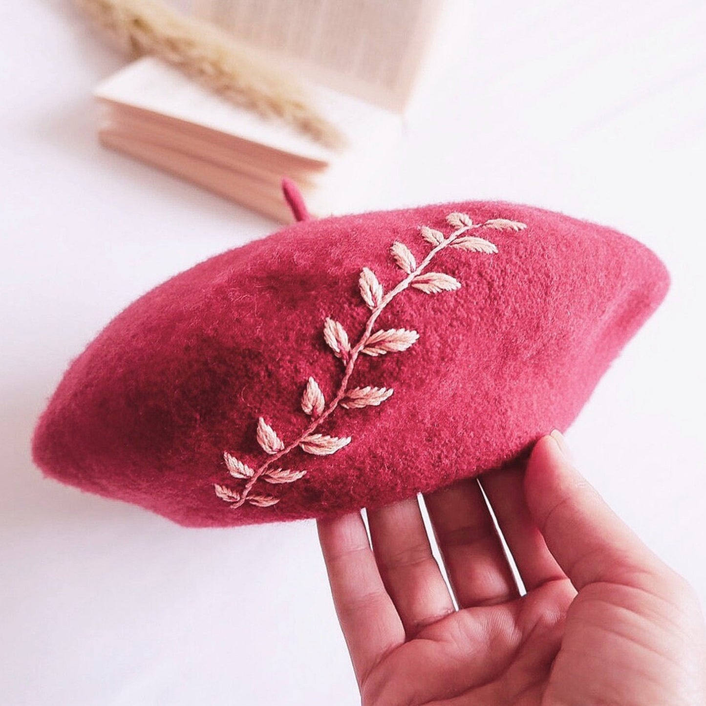 Red beret with floral embroidery held by a hand on a light background