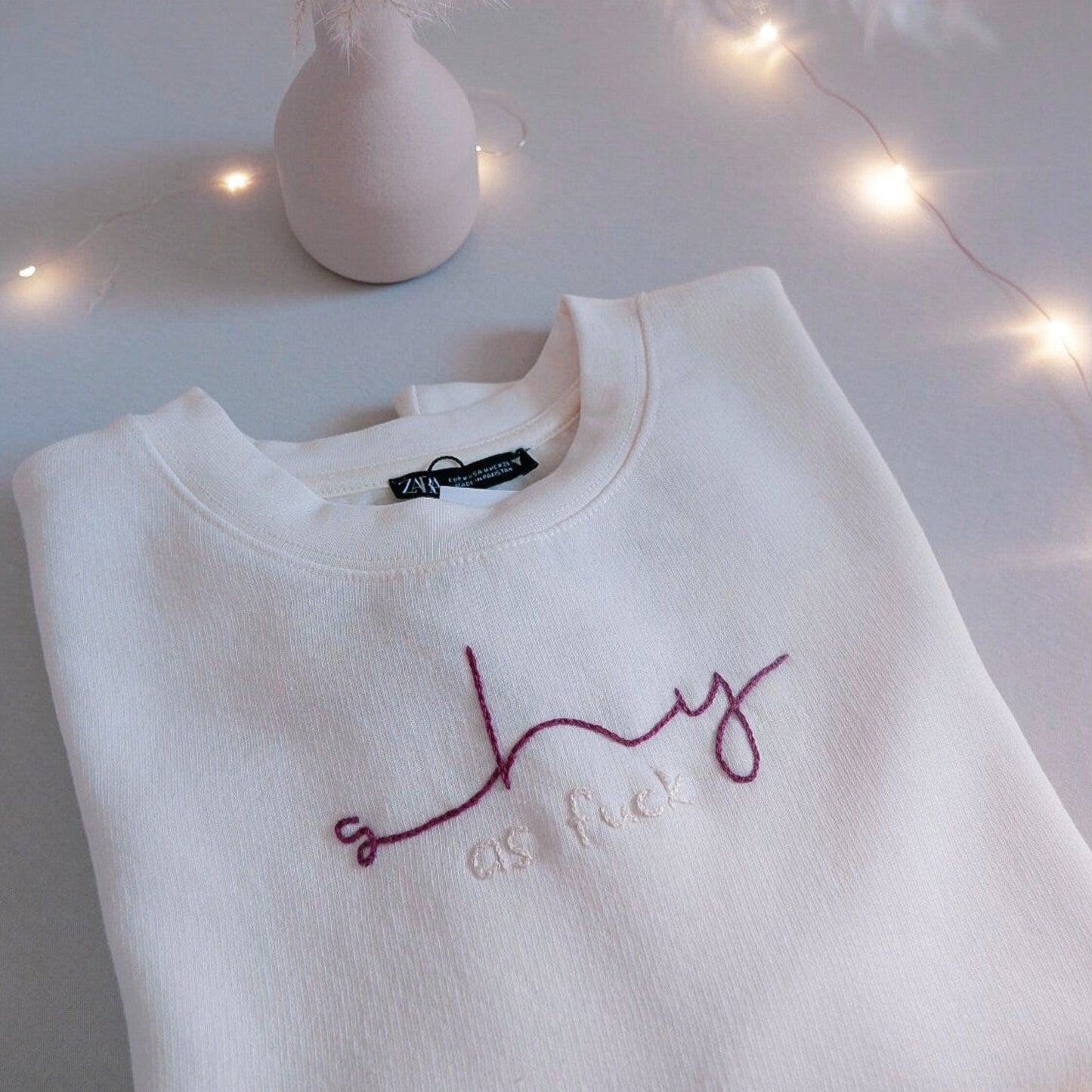 White sweatshirt with embroidered text on a light surface with decorative elements
