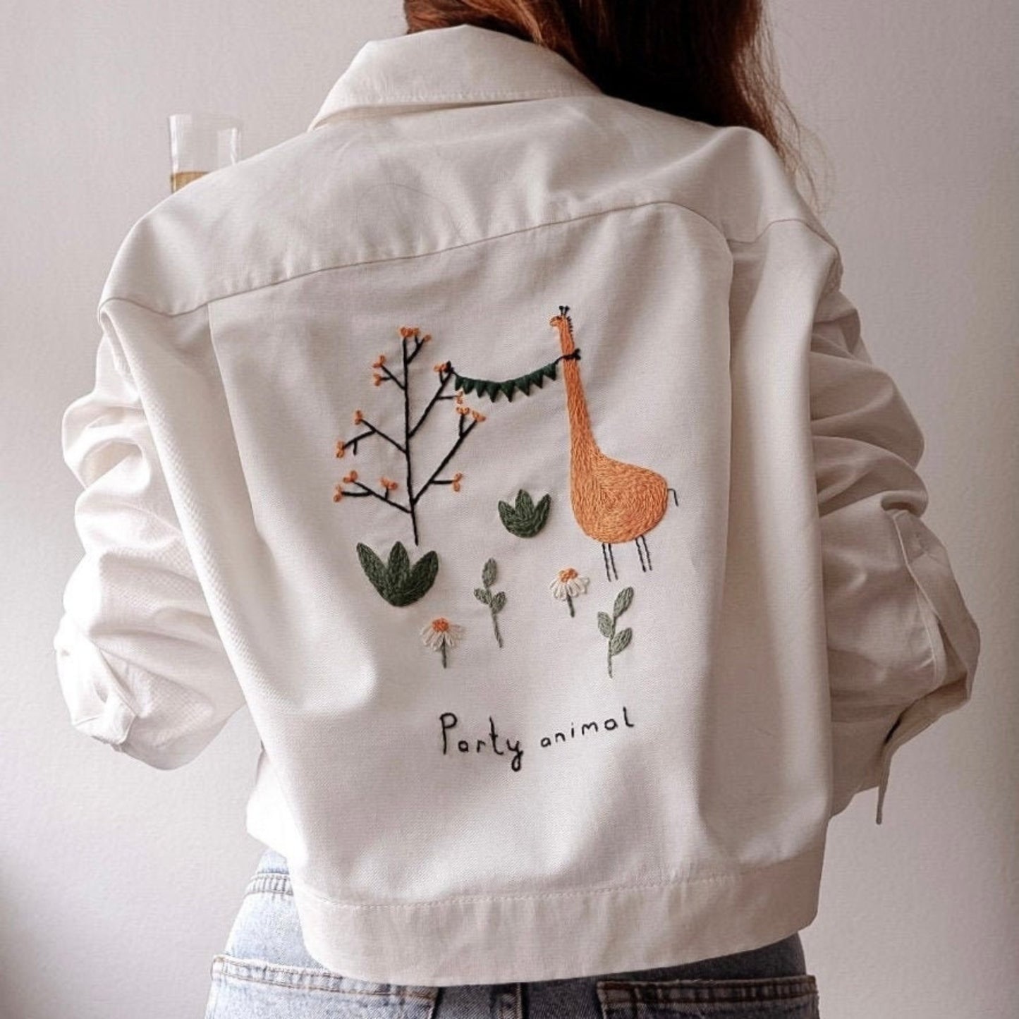 White denim jacket with giraffe and plant embroidery on a plain background