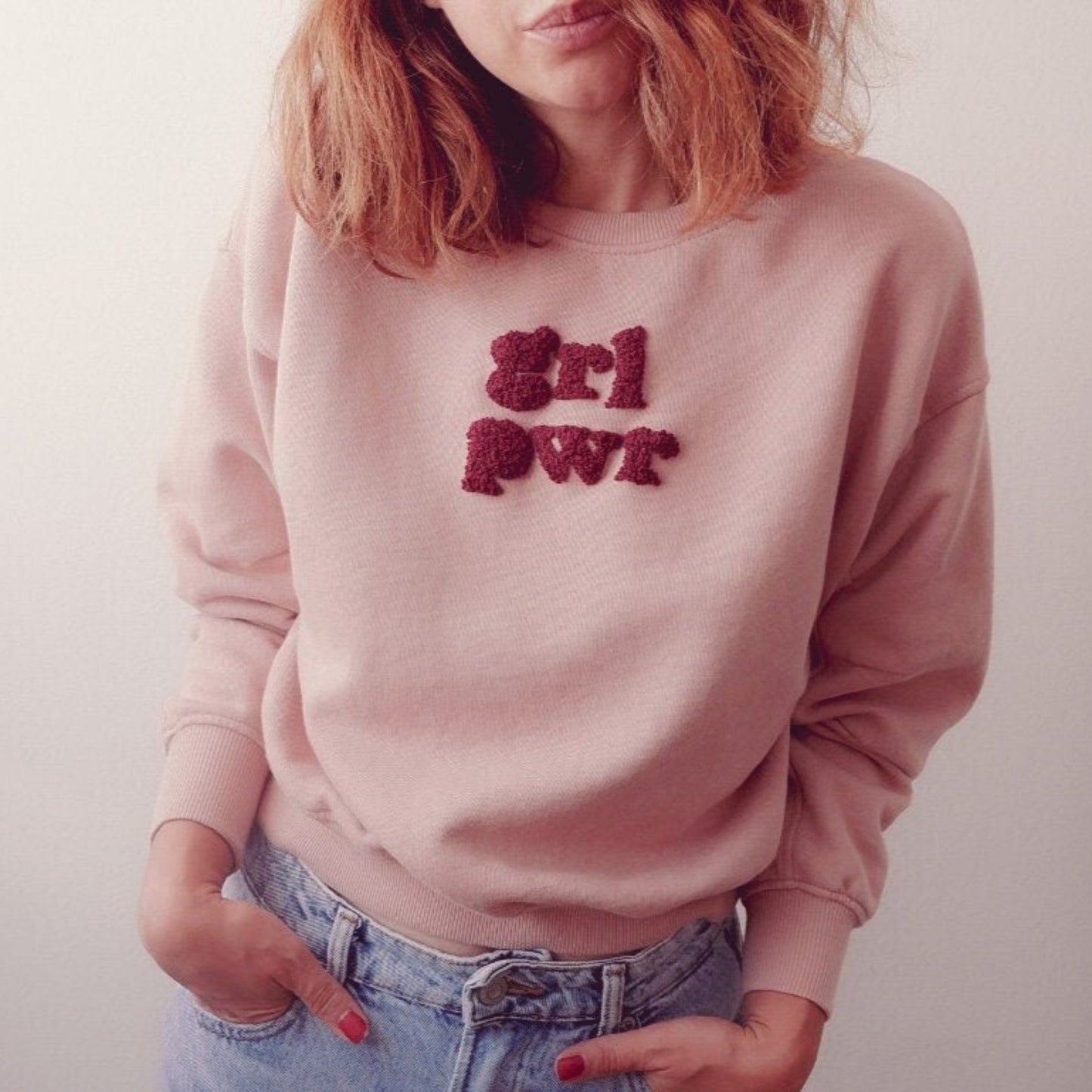 Person wearing a pink sweatshirt with 'Girl Pwr' text, standing against a plain background