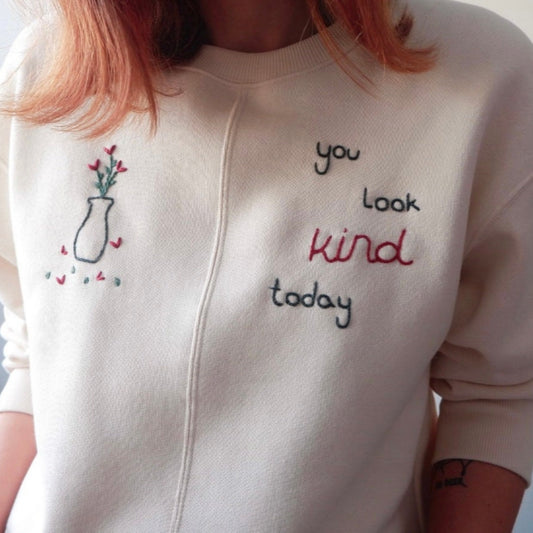 White sweatshirt with embroidered text and design on a plain background