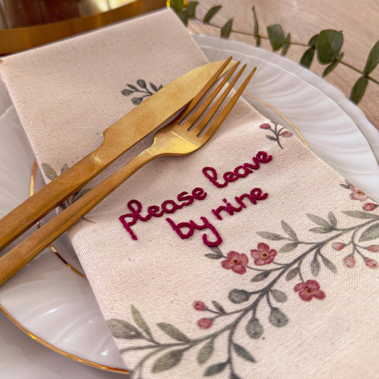 Napkin with 'Please leave by nine' text on a table setting with cutlery.