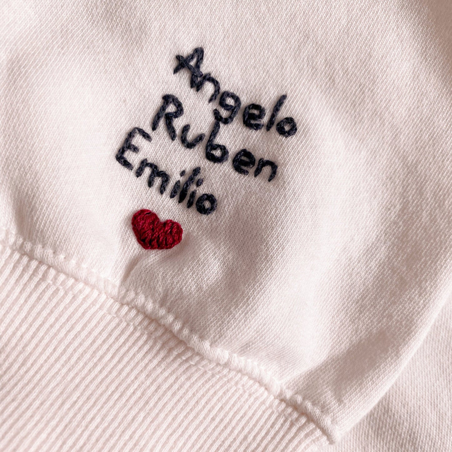 White fabric with embroidered names and a red heart design