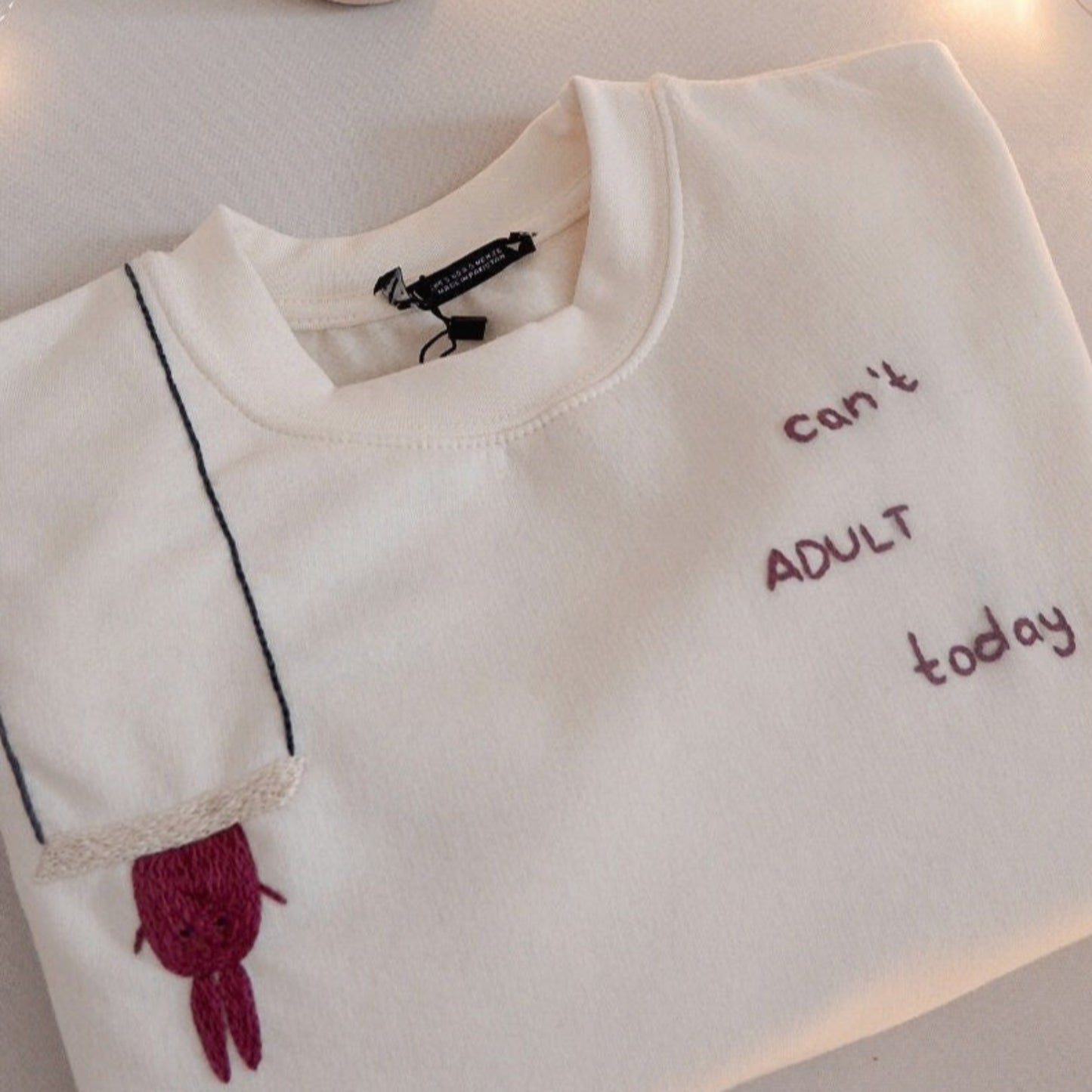White sweatshirt with text and owl design on a white surface with fairy lights