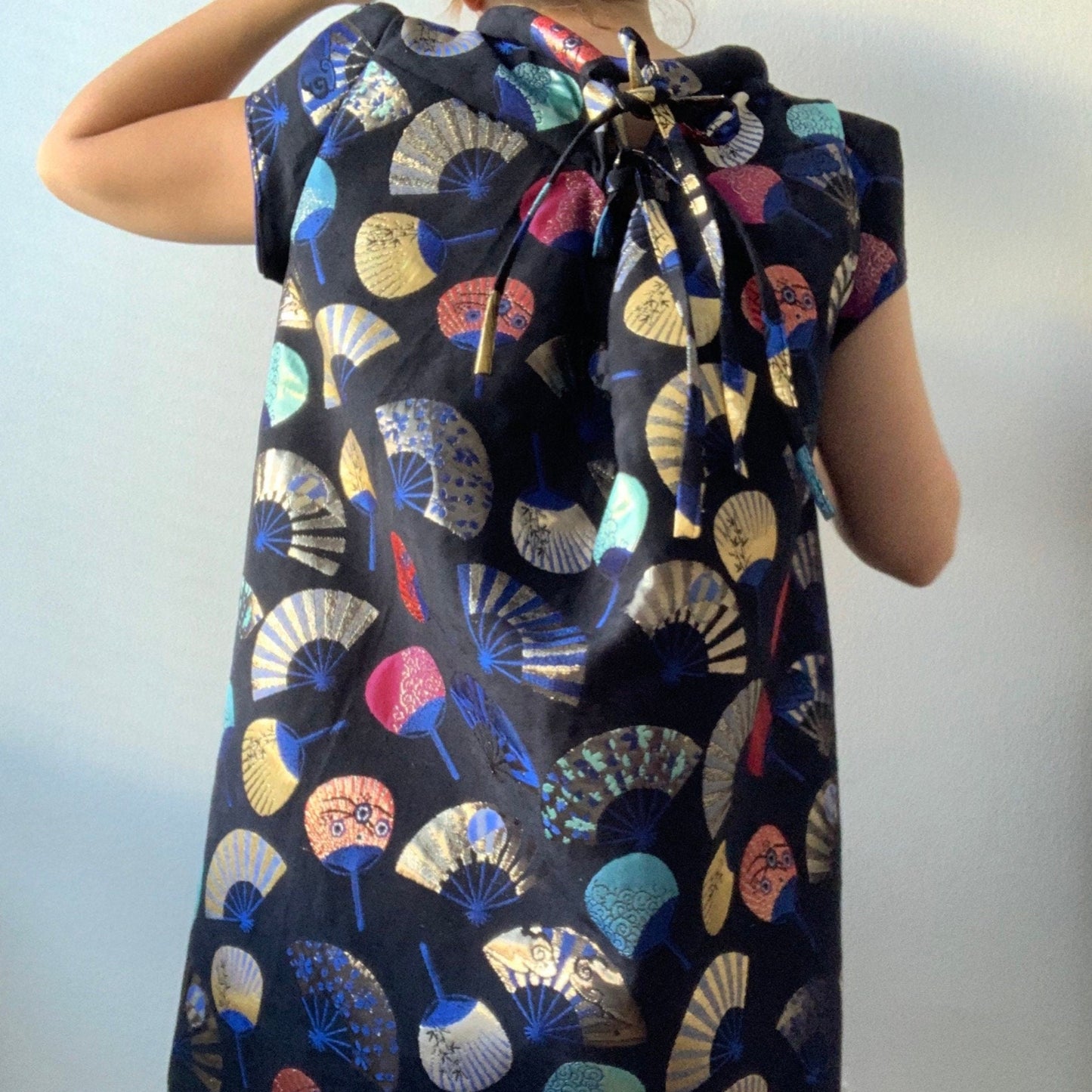 Woman wearing a dress with colorful fan pattern on a plain background