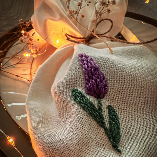Embroidered lavender flower on a white fabric with blurred lights in the background