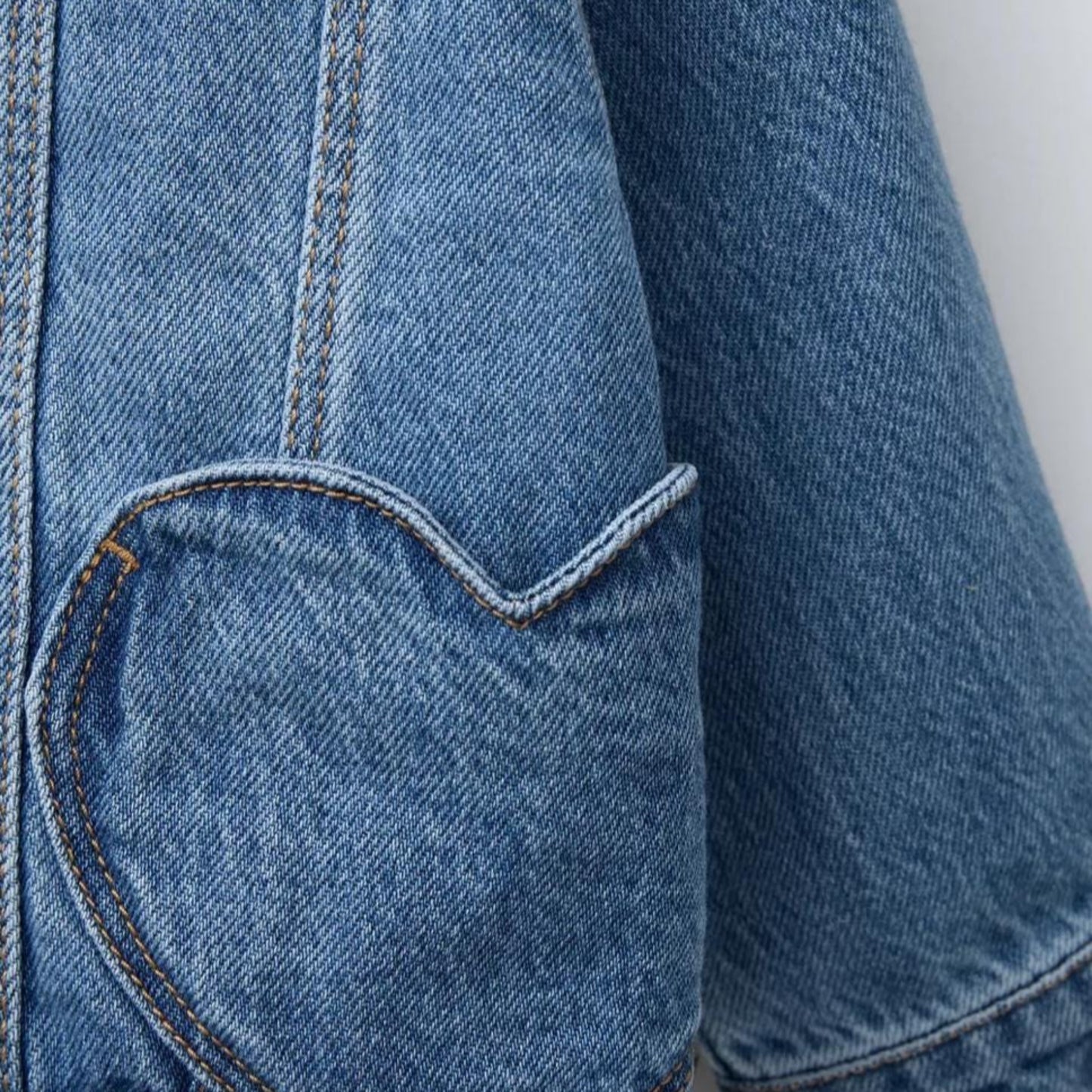 Close-up of a blue denim jacket with a heart-shaped pocket on a light gray background