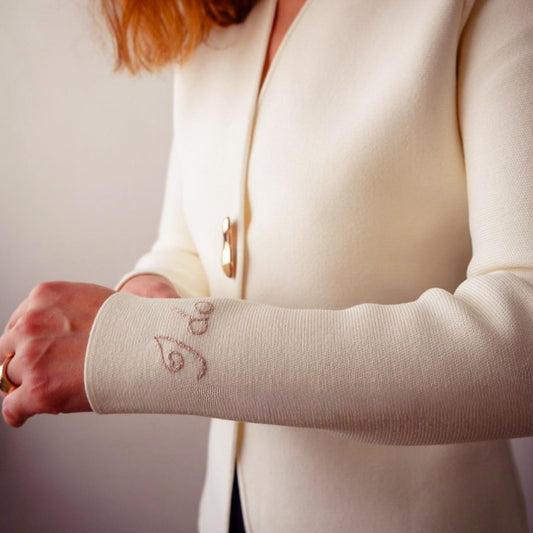 Person wearing a beige arm sleeve with embroidered designs on a plain background