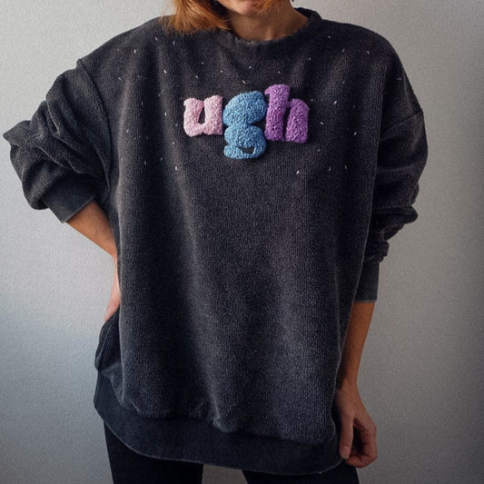 Person wearing a dark gray sweatshirt with colorful text on a plain background