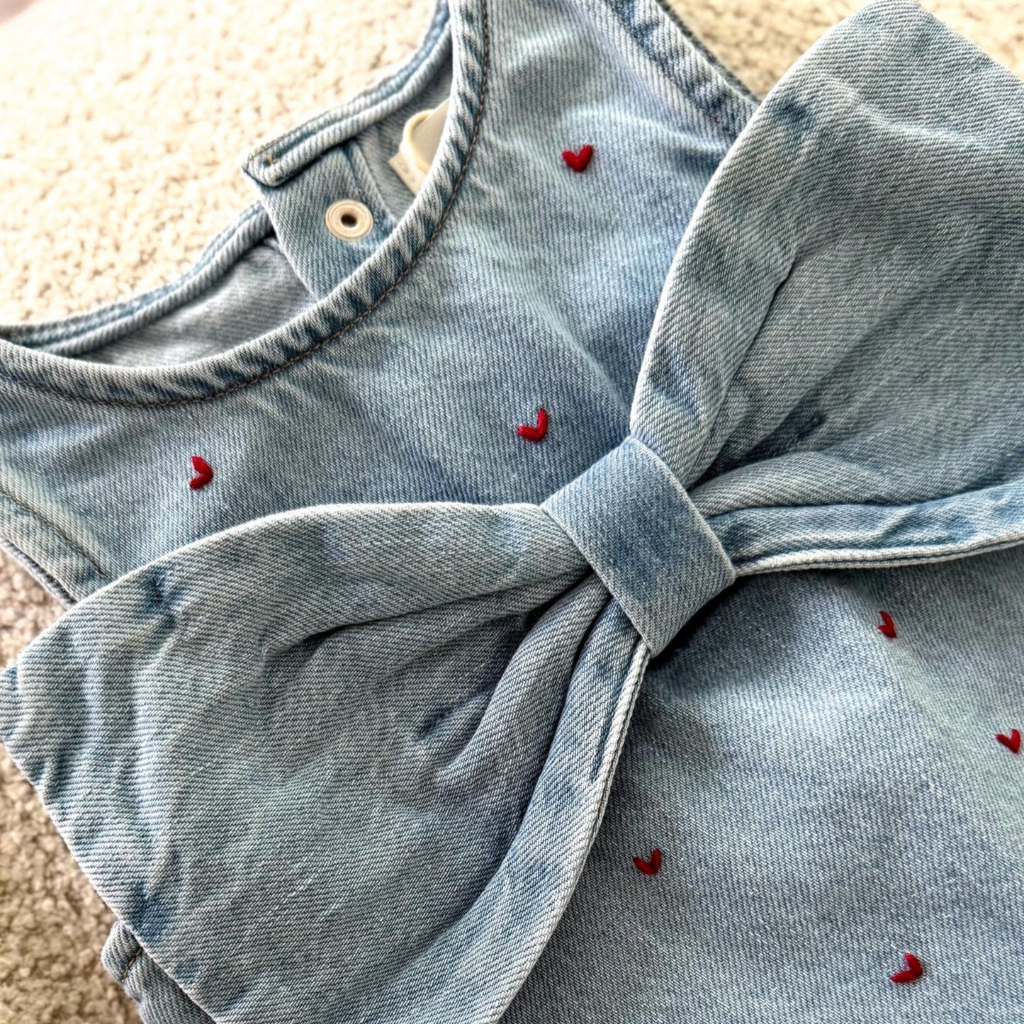 Light blue denim dress with a large bow detail on a beige surface