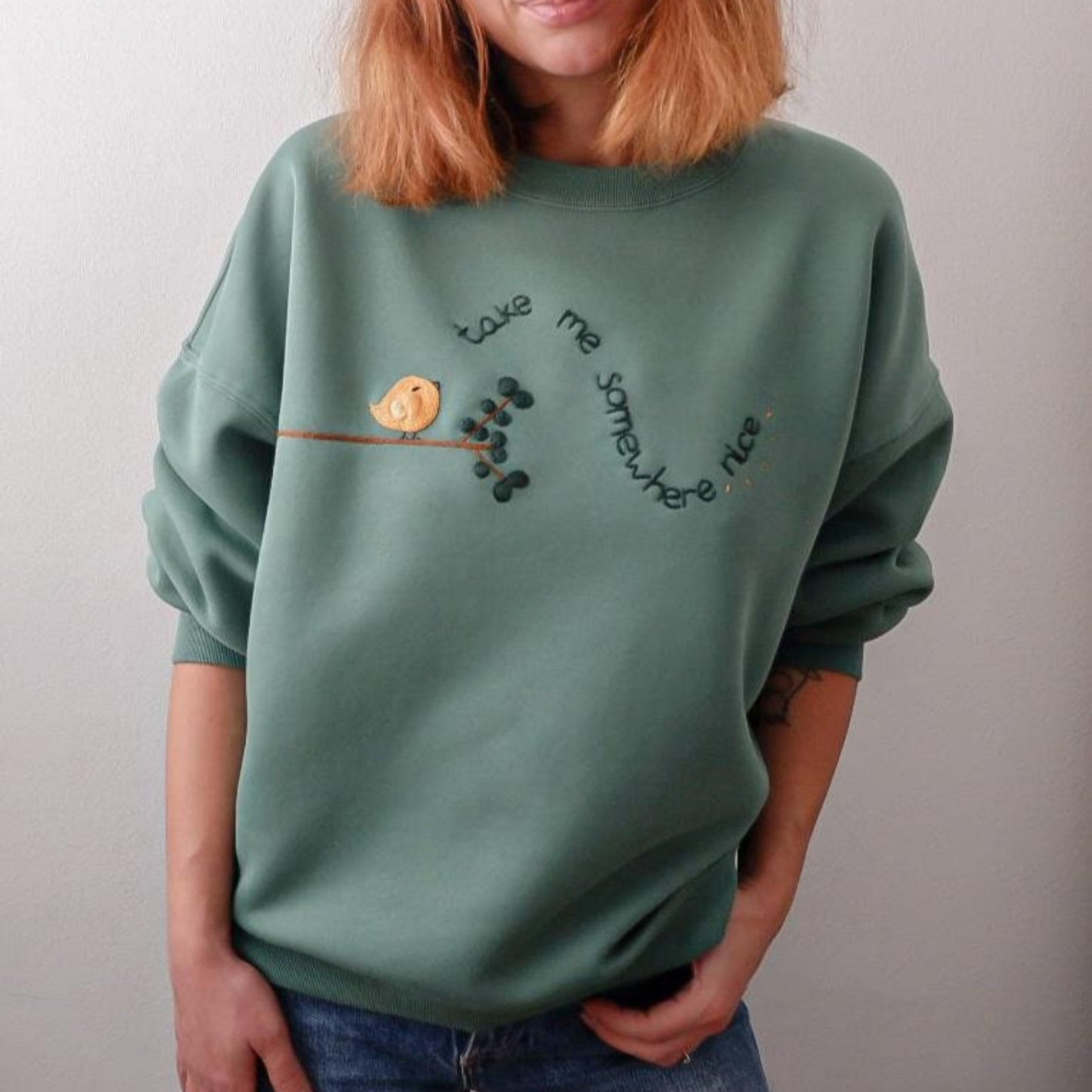 Person wearing a green sweatshirt with a bird and branch design on a plain background