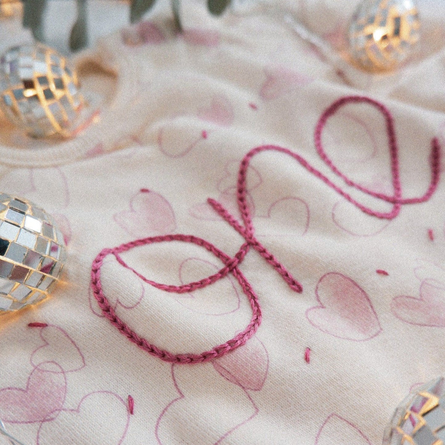 Baby blanket with 'one' embroidered in pink on a white background with heart patterns.