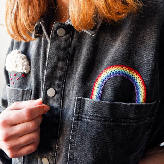 Person wearing a denim jacket with a rainbow patch on the chest pocket.