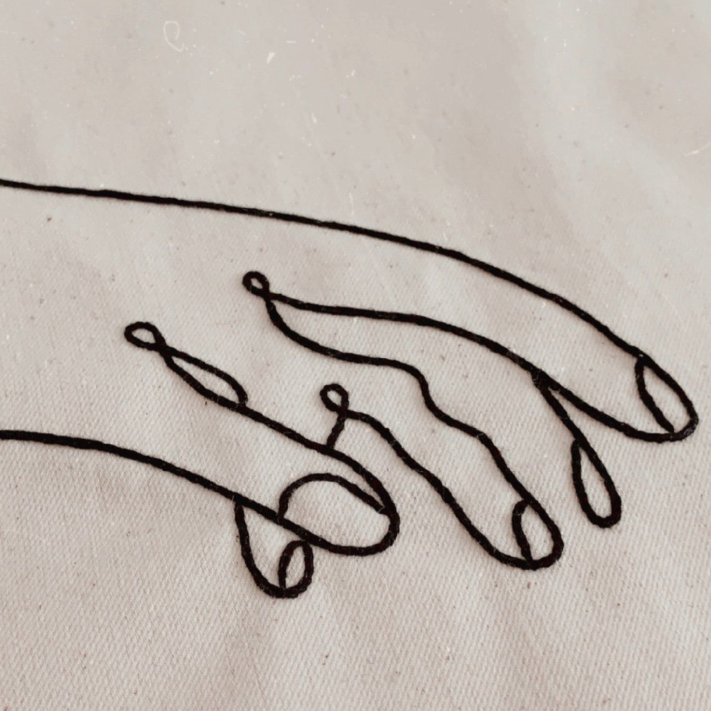 Embroidered design of two hands on a beige fabric background