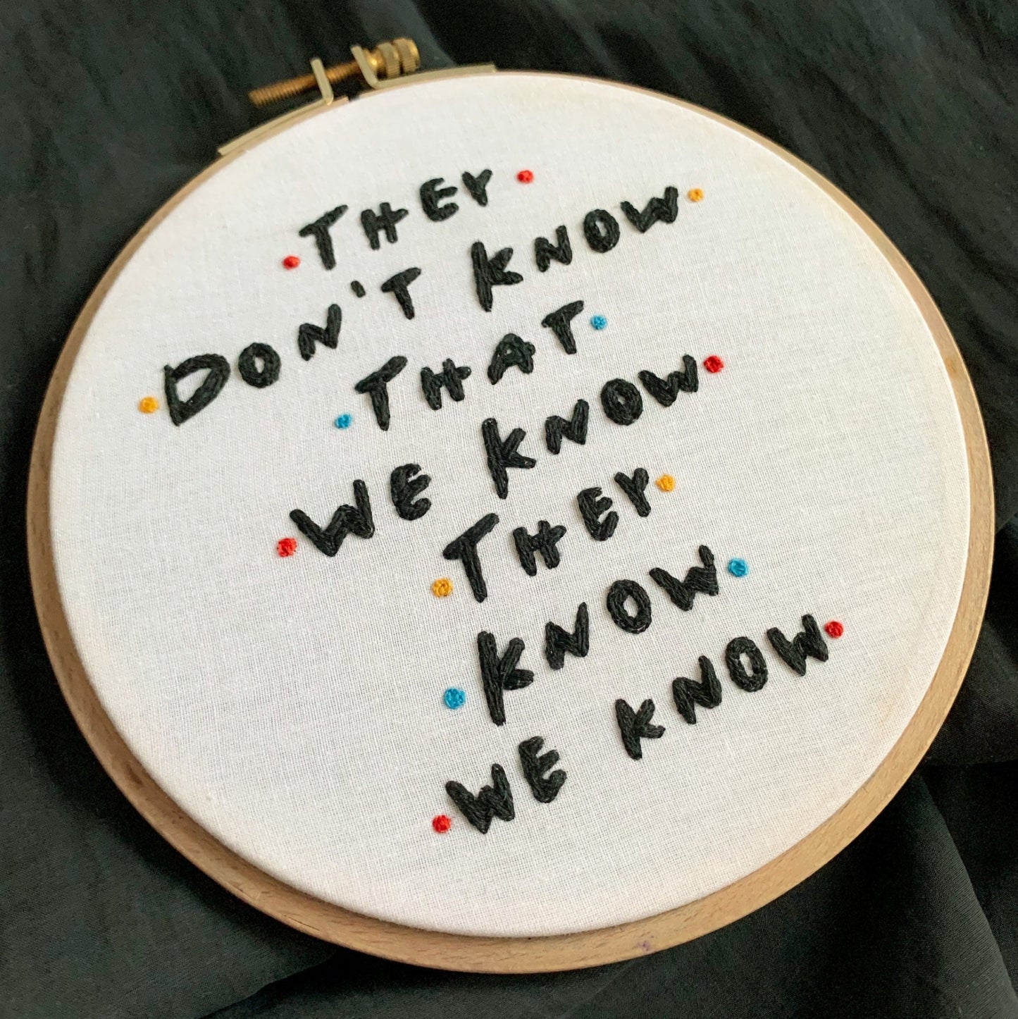 Embroidery hoop with text 'They don't know that we know they know we know' on a dark fabric background