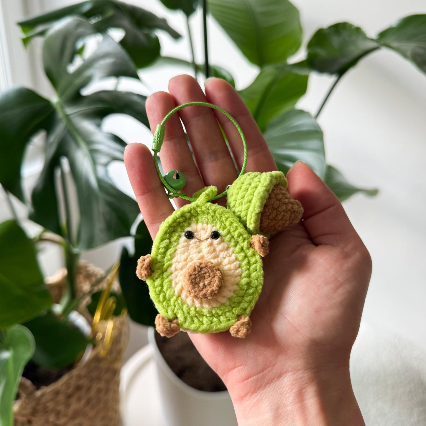 Hand holding a avocado crochet keychain with a plant in the background
