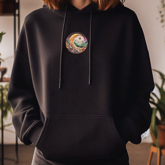 Person wearing a black hoodie with a colorful design on the chest in an indoor setting with plants.