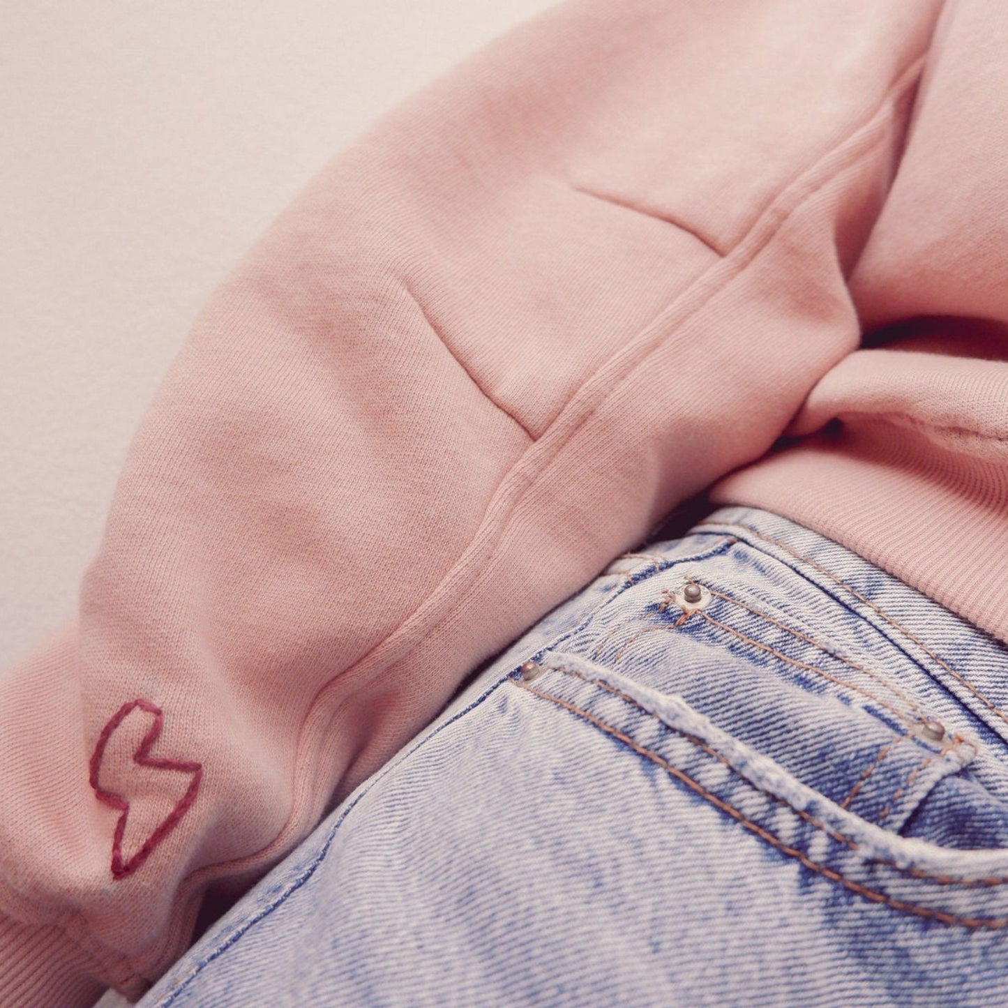 Pink hoodie with a red heart design on sleeve and blue jeans.