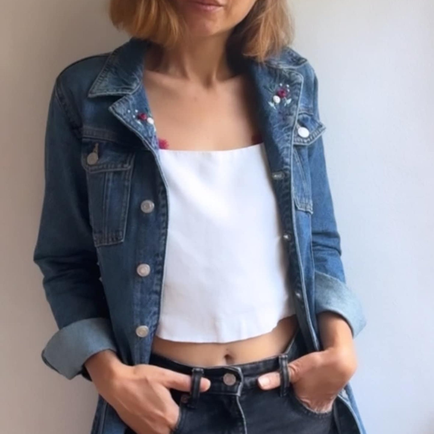 Person wearing a denim jacket, white crop top, and black shorts against a plain background