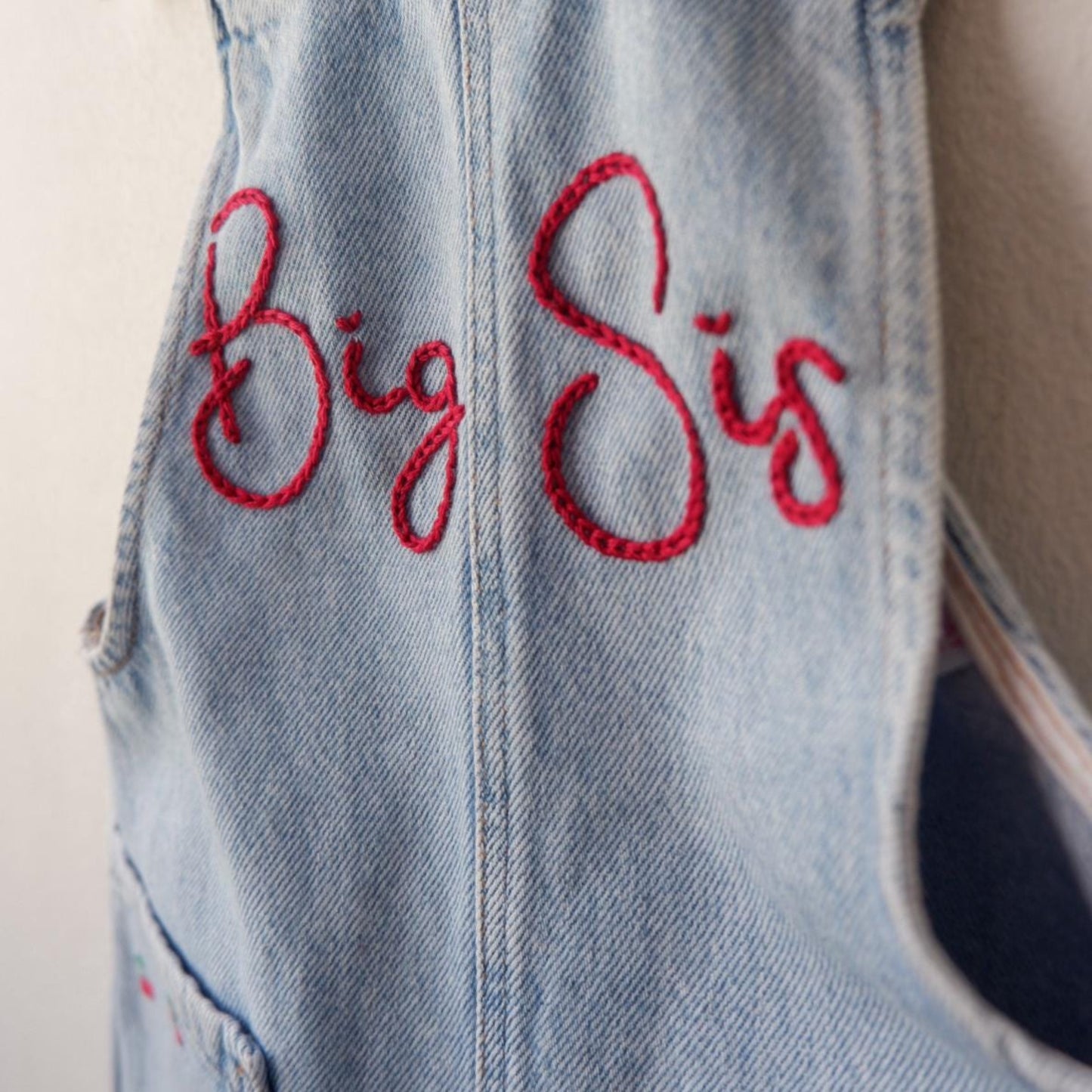 Denim overalls with 'Big Sis' embroidered in red on a plain background