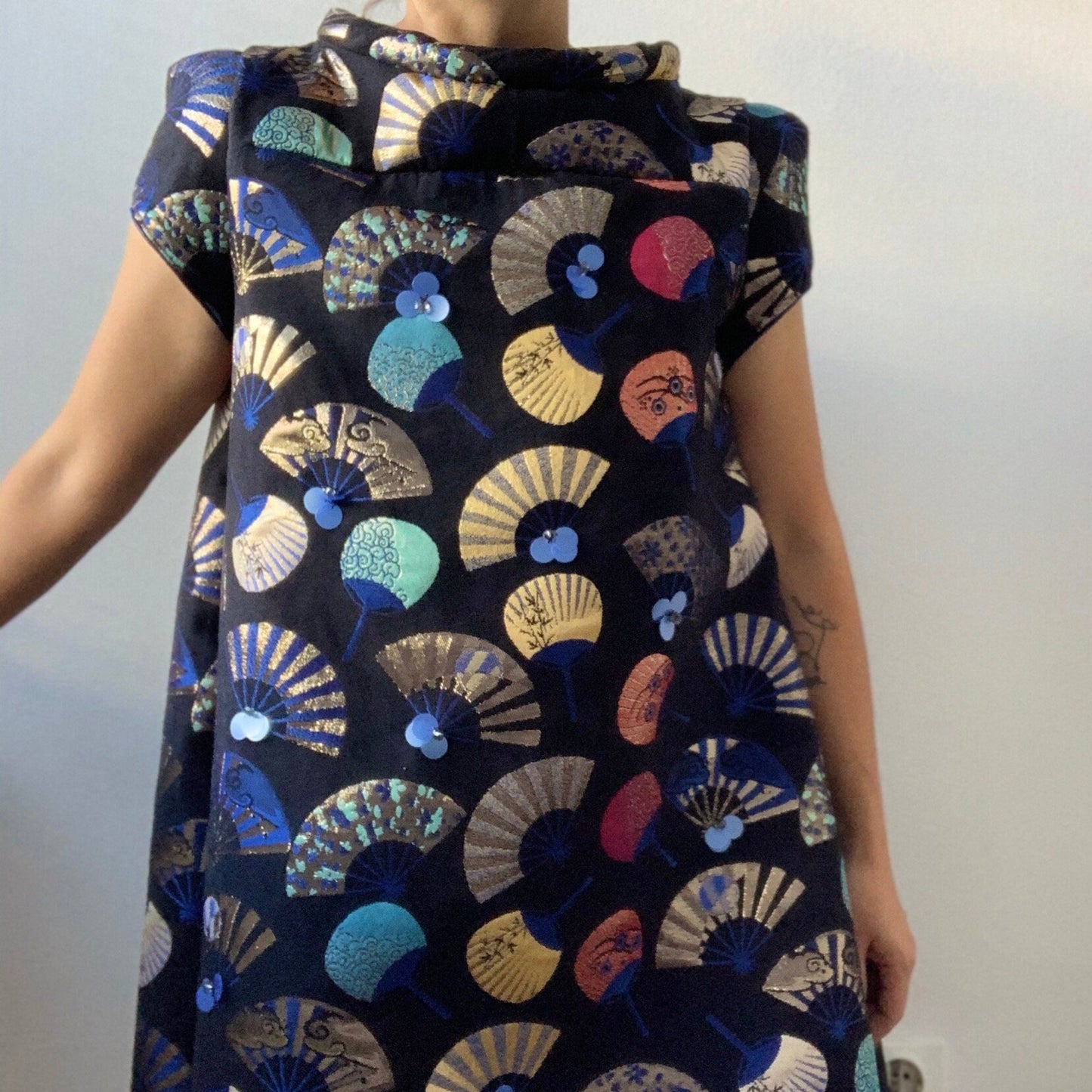 Person wearing a sleeveless dress with colorful geometric pattern on a plain background
