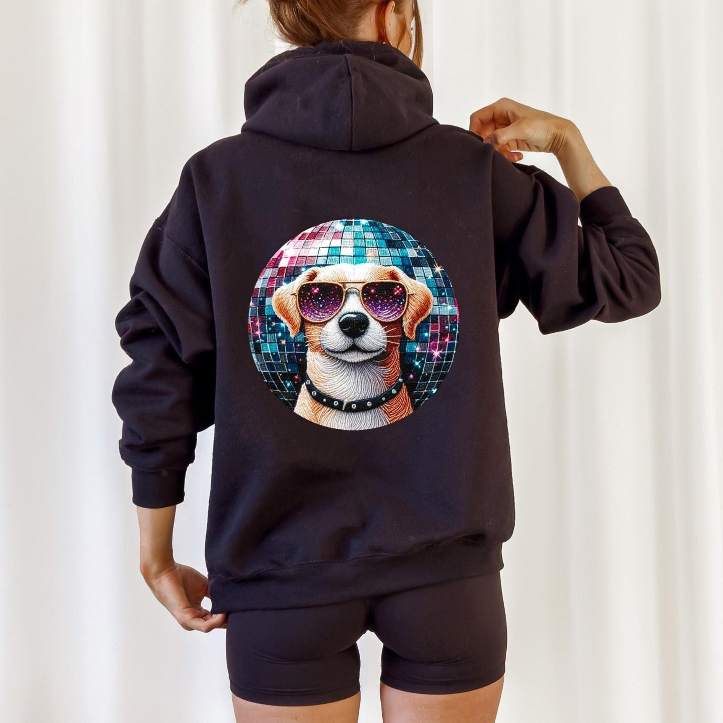 Person wearing a black hoodie with a colorful dog design on the back against a white curtain background