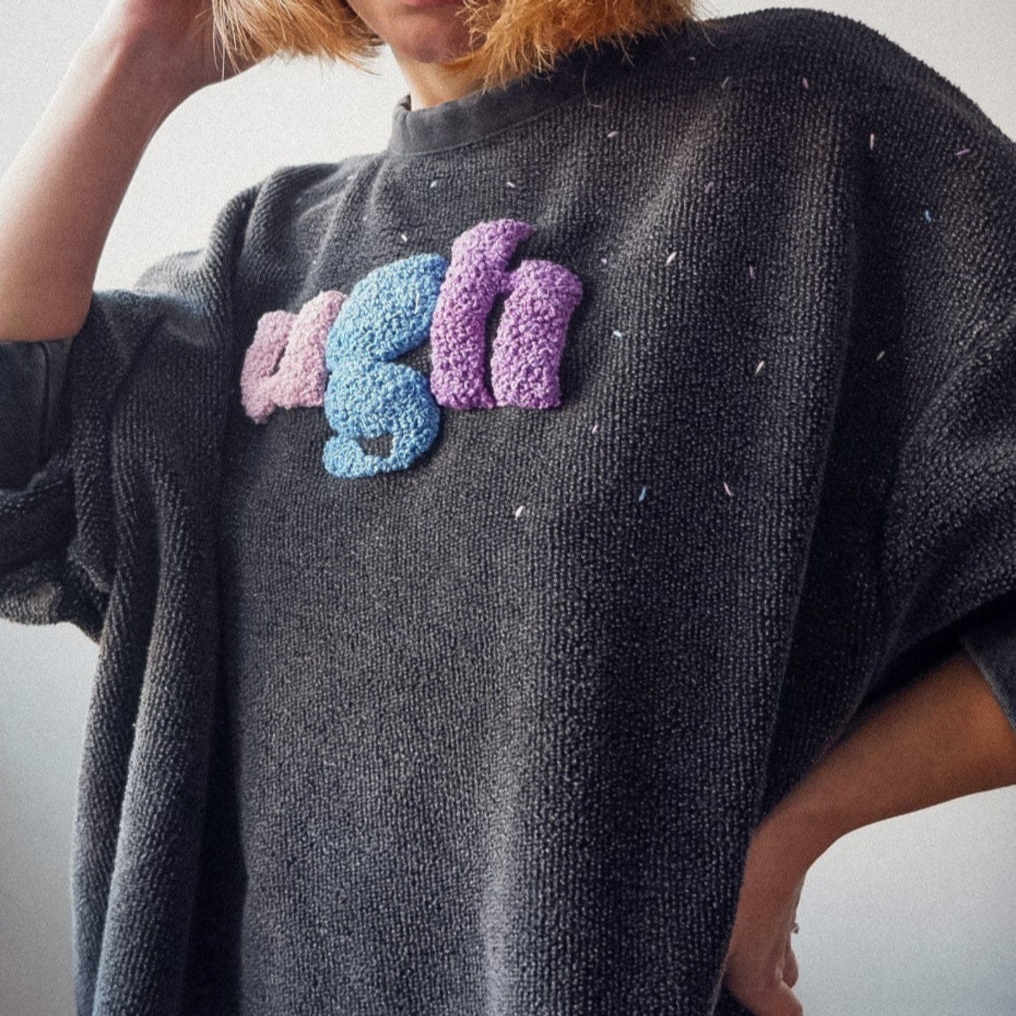 Person wearing a dark gray sweater with colorful snake design on a light background
