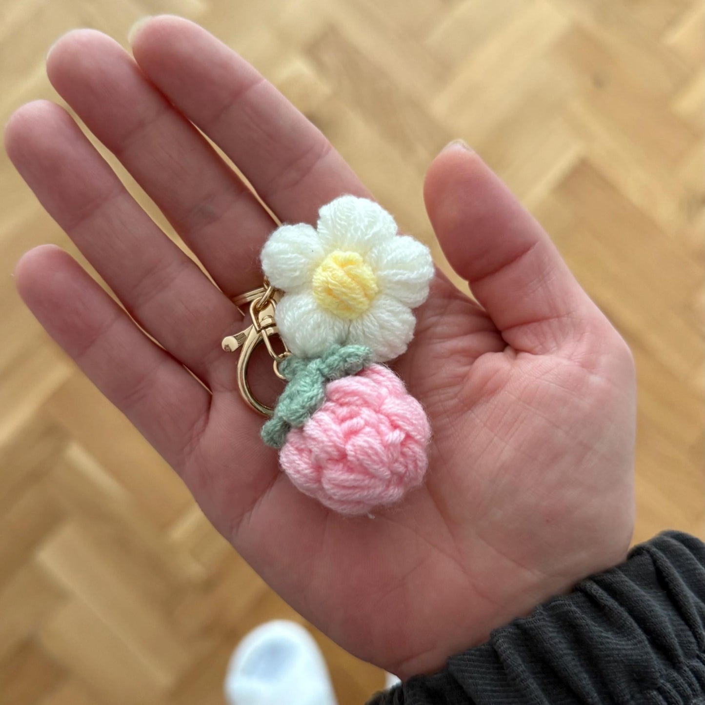 Hand holding a small crocheted flower and ball of yarn against a wooden background
