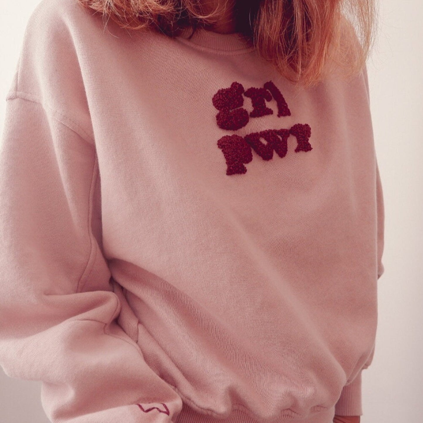 Pink sweatshirt with red text worn by a person, on a plain background