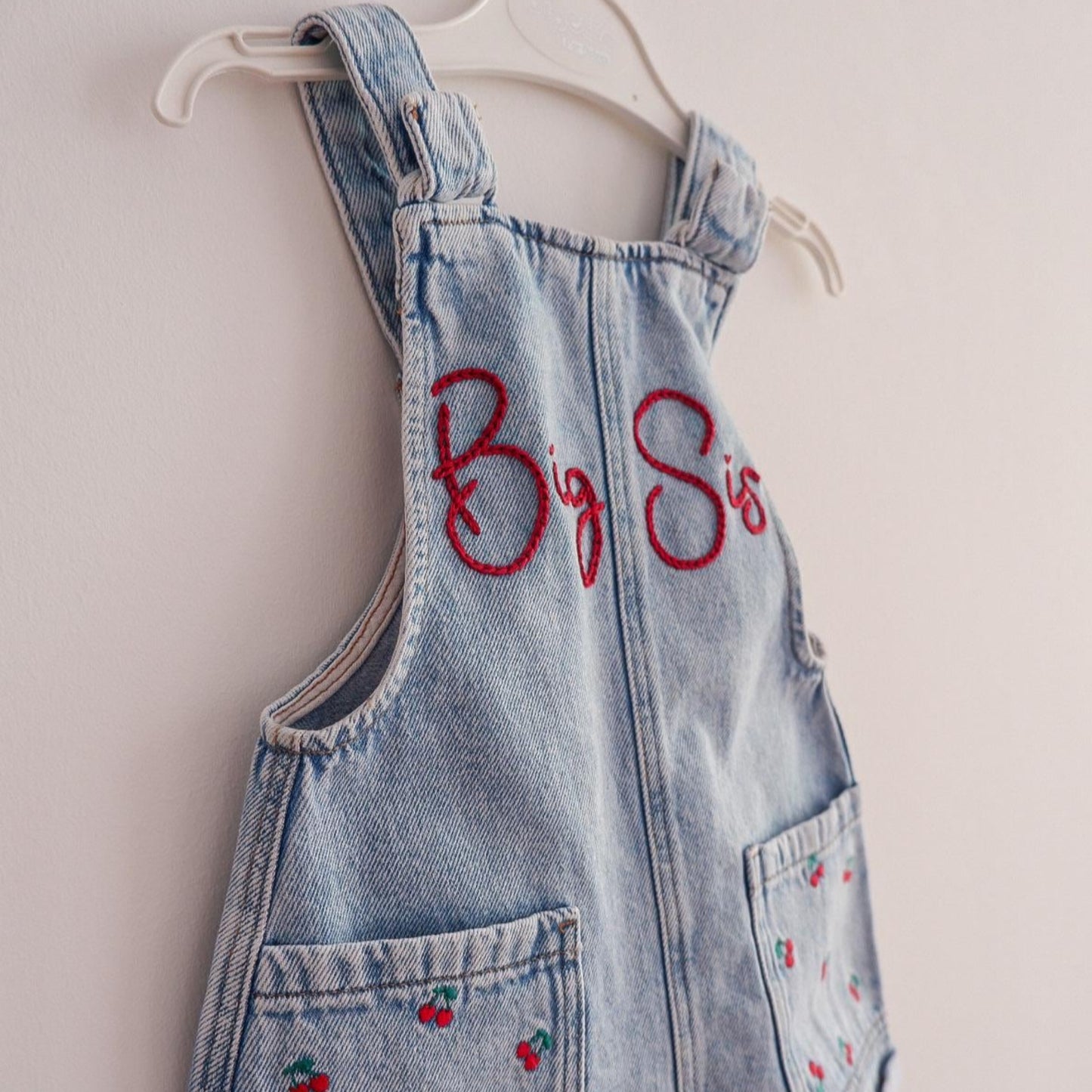 Denim overall dress with red embroidery on a white background