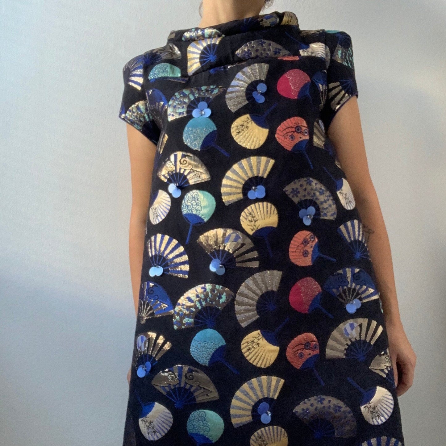Woman wearing a black dress with colorful fan pattern against a plain background