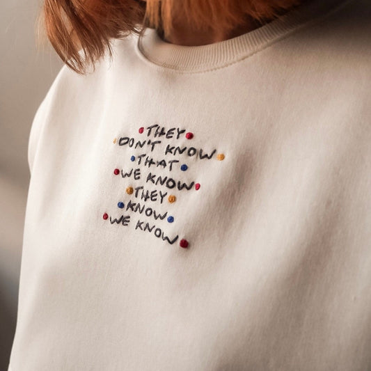 White sweatshirt with embroidered text and colorful dots on a neutral background