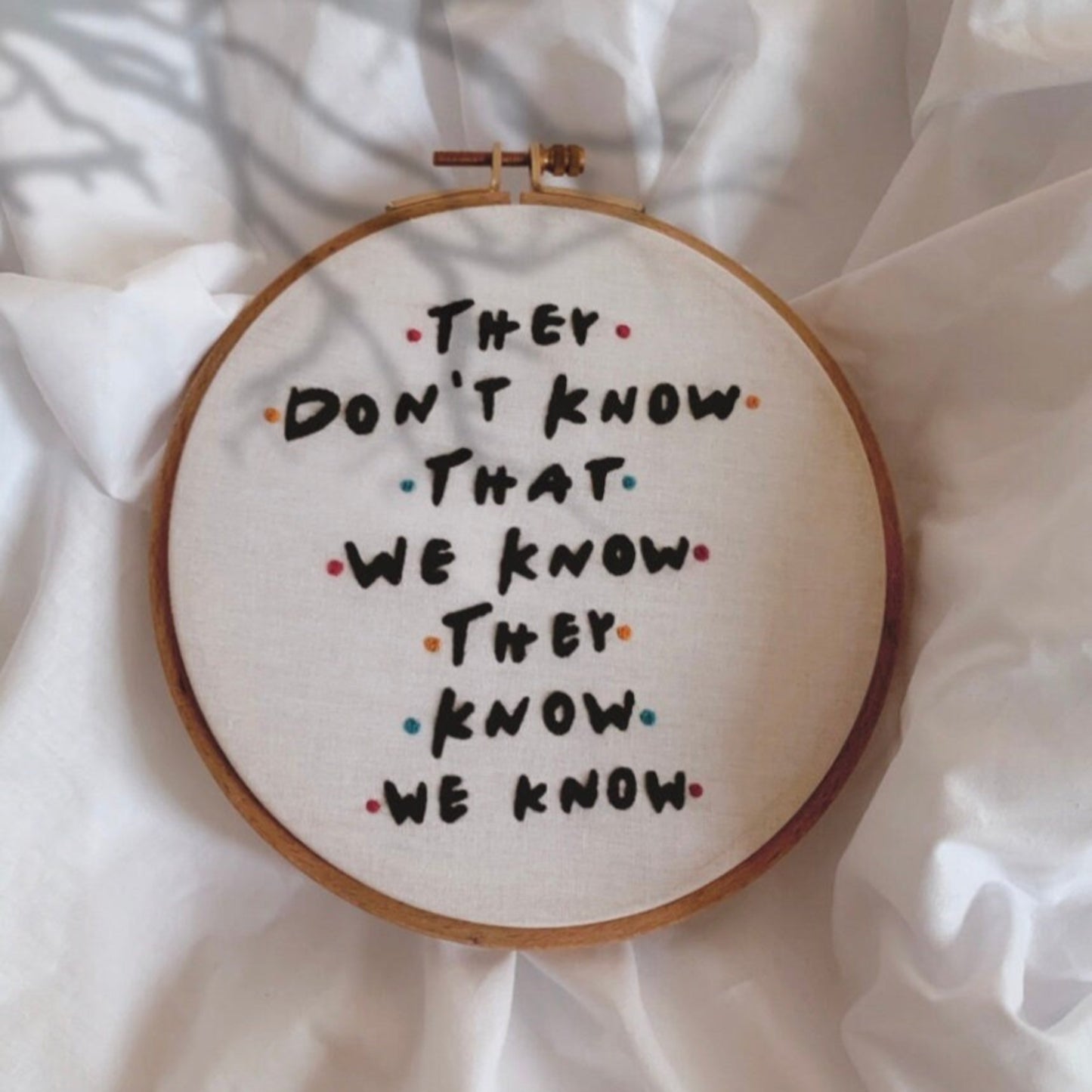 Embroidery hoop with text 'They don't know that we know they know we know' on a white fabric background