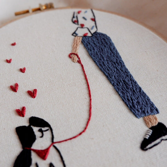 Embroidery hoop with a person and dog illustration, hearts, and a red leash.