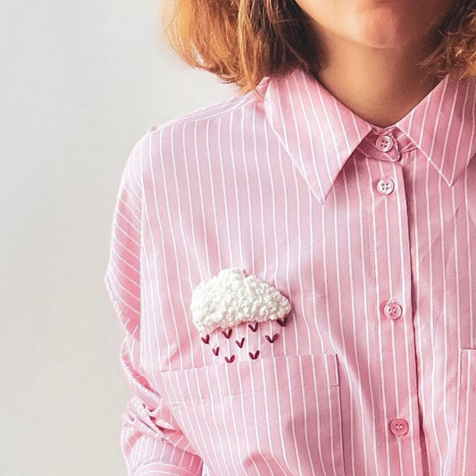 Person wearing a pink striped shirt with a decorative cloud and raindrop brooch.