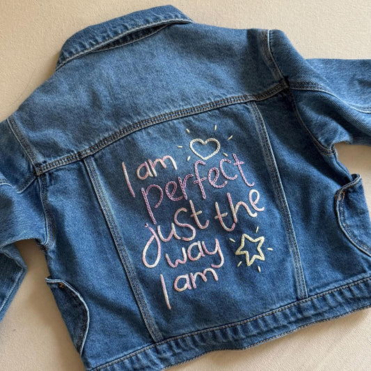 Denim jacket with embroidered text on a beige background