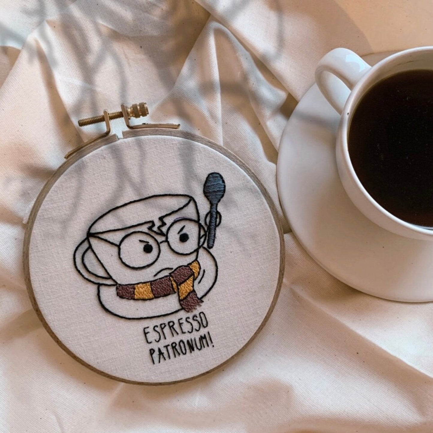 Hand embroidery hoop art depicting a coffee cup with the text 'ESPRESSO PATRONUM' on a wall, next to a cup of coffee.