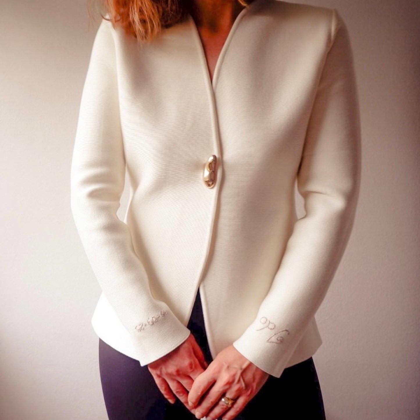 White blazer with a gold button worn by a person against a plain background