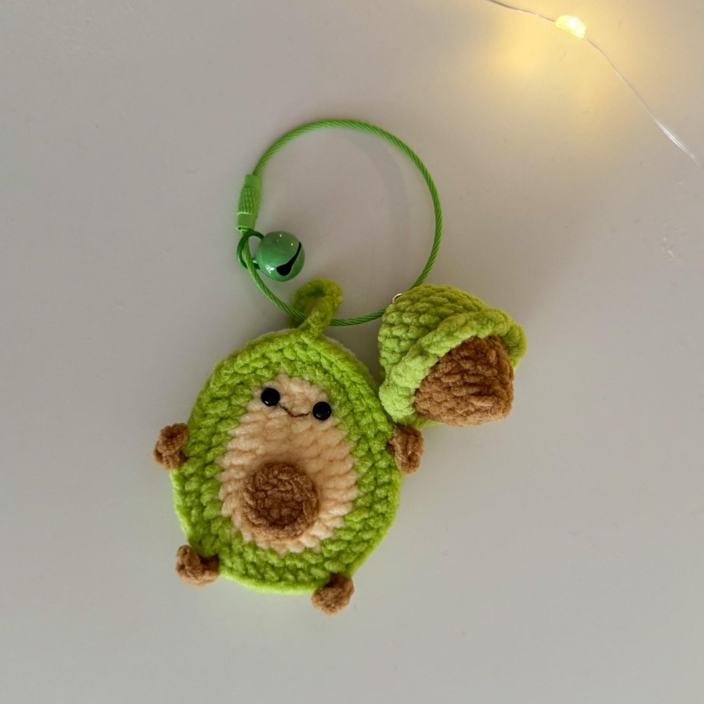 Crocheted avocado-shaped keychain with a bell on a white background