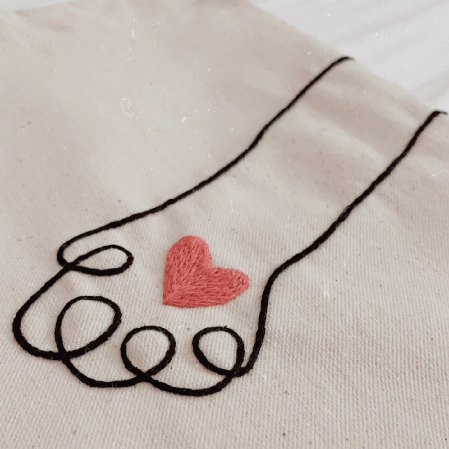 Embroidered design of a hand holding a heart on a beige fabric background