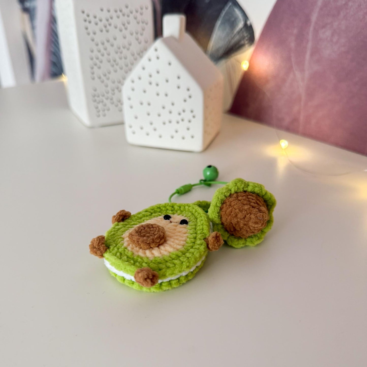 Green and brown crocheted avocado plush toy on a white surface with decorative items in the background.