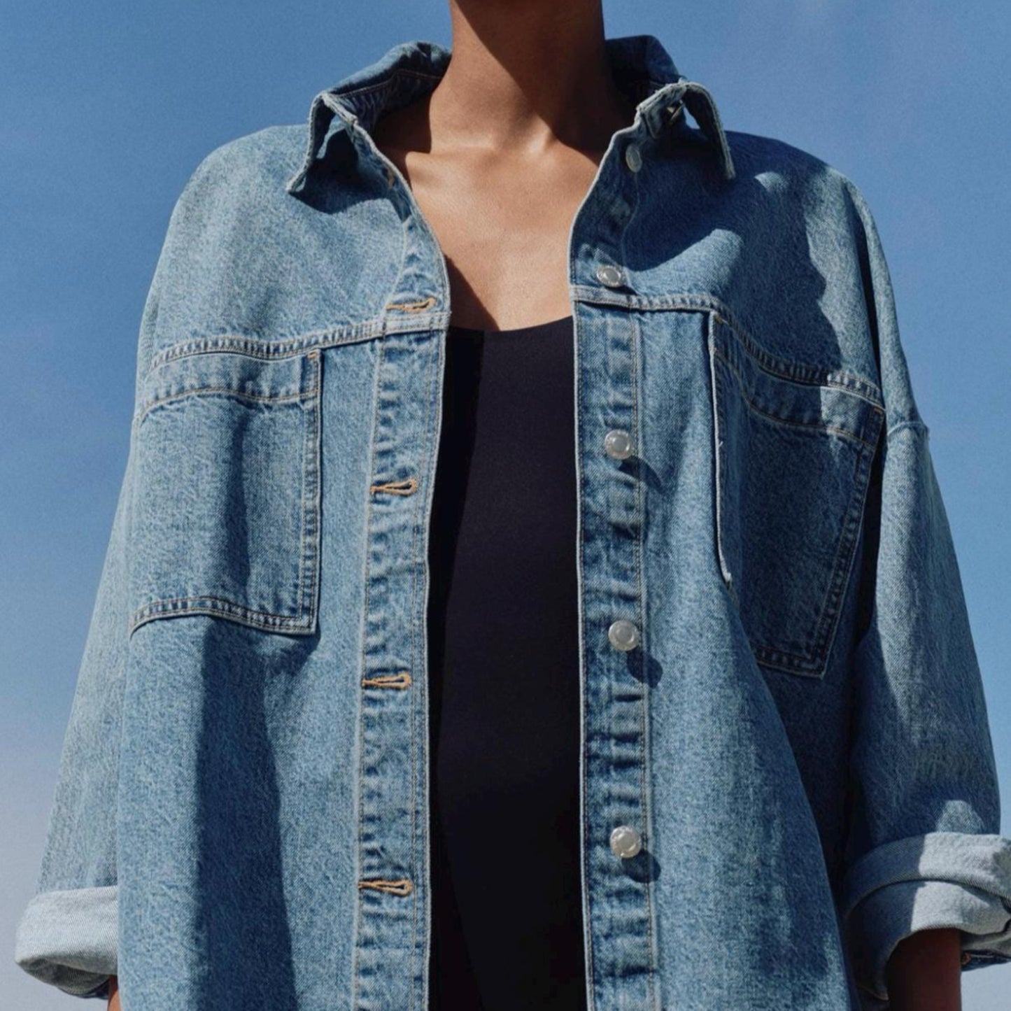 Person wearing a denim jacket against a clear blue sky