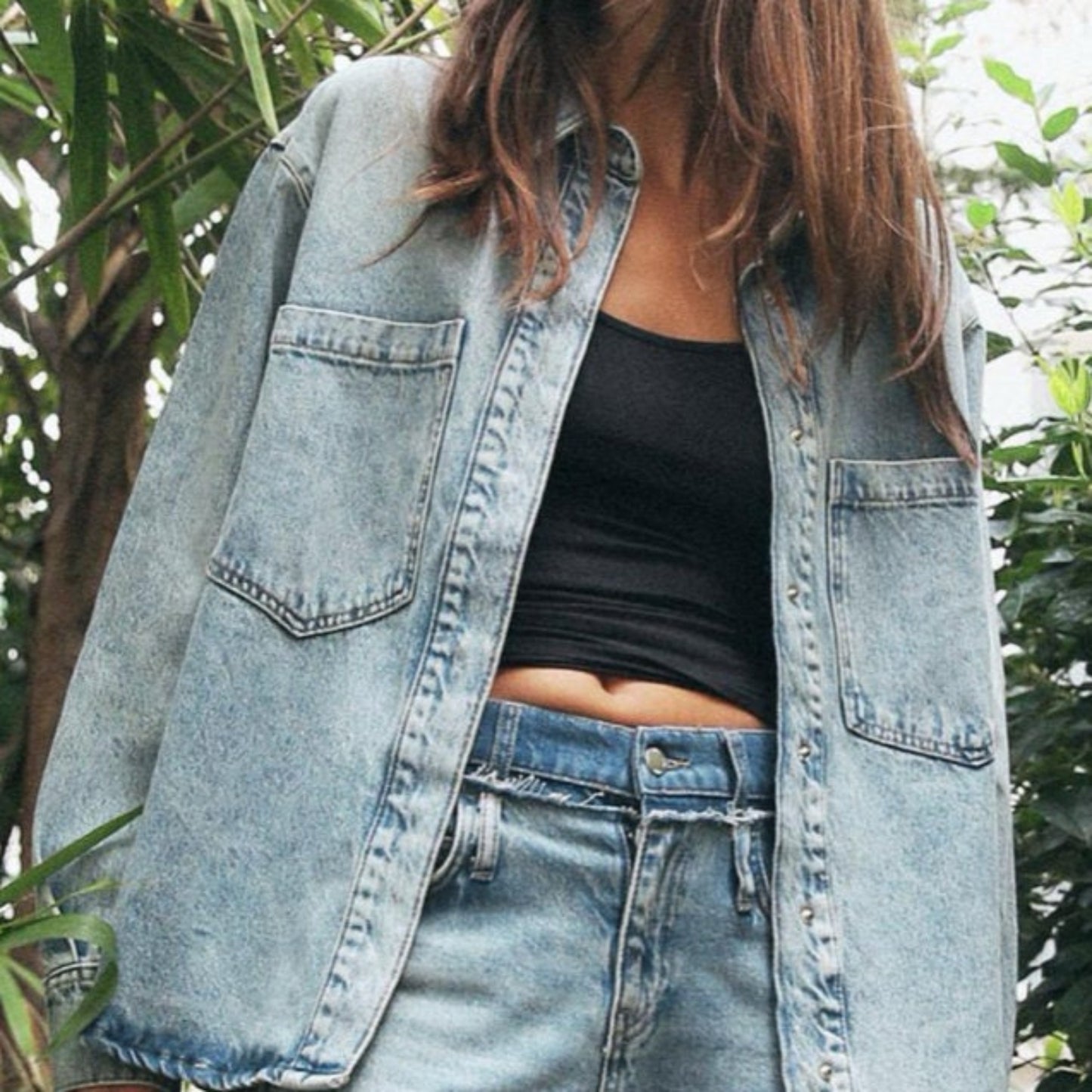 Person wearing a light blue denim jacket and jeans with a blurred natural background